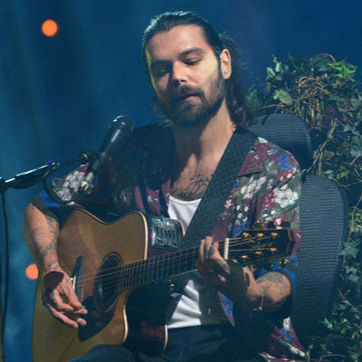 Man playing guitar on stage with microphone and plants in the background